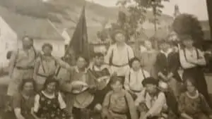 Historisches Foto: eine Gruppe in Trachten mit Musikinstrumenten und einer Fahne im Freien